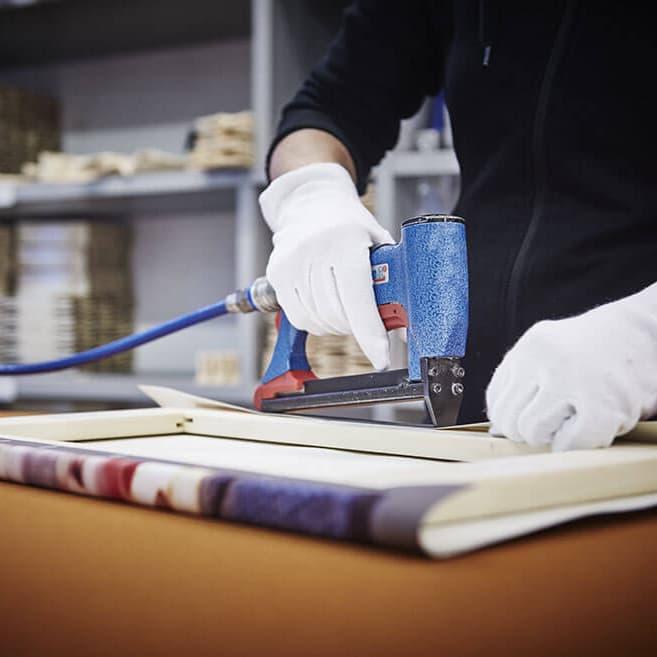 Leidenschaftliche Handarbeit in unserer Werkstatt Mitarbeiterin spannt eine Leinwand in der Posterkoenig Werkstatt